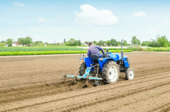 farmer on a tractor with a cultivator processes a farm field. soil preparation, cutting of rows for planting crop plants. farming agribusiness. agricultural industry. growing vegetables food plants.