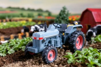 Petit tracteur gris sur terre cultivée avec ferme en arrière-plan